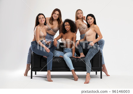 Group of women with different body types in jeans and underwear on sofa against light background 96146003