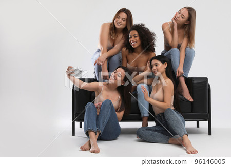 Group of women with different body types in jeans and underwear taking selfie against light 96146005
