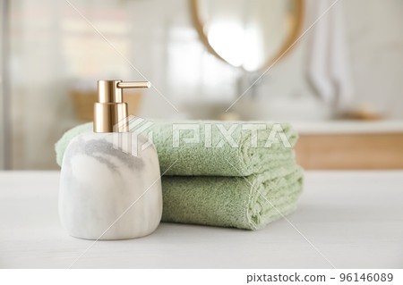 Clean towels and soap dispenser on white wooden table in bathroom 96146089