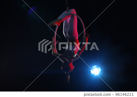 Young woman performing acrobatic element on aerial ring against dark background 96146221