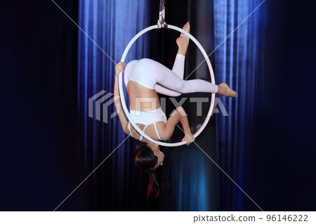 Young woman performing acrobatic element on aerial ring indoors 96146222