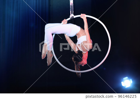 Young woman performing acrobatic element on aerial ring indoors 96146225