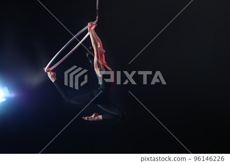 Young woman performing acrobatic element on aerial ring against dark background. Space for text Young woman performing acrobatic element on aerial ring against dark background. Space for text 96146226
