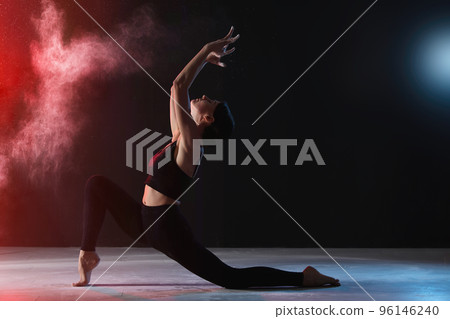 Professional acrobat with chalk powder exercising in dark studio 96146240