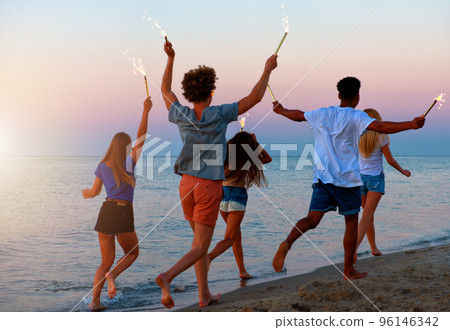 Happy smiling friends running at the beach with sparkling candles 96146342