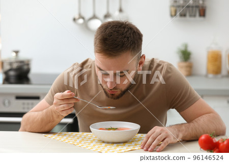 Young man eating tasty vegetable soup at table in kitchen 96146524