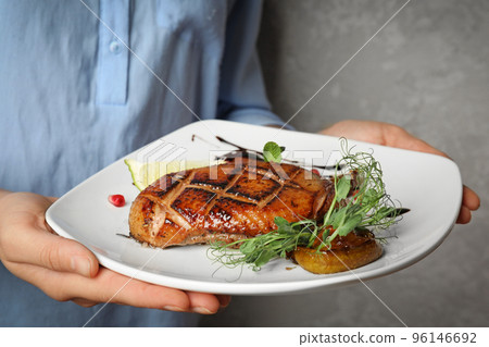 Woman holding plate with grilled duck breast on grey background, closeup Woman holding plate with grilled duck breast on grey background, closeup 96146692