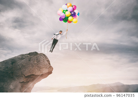 Creative businessman holding colorful balloons flies from the peak of a mountain 96147035