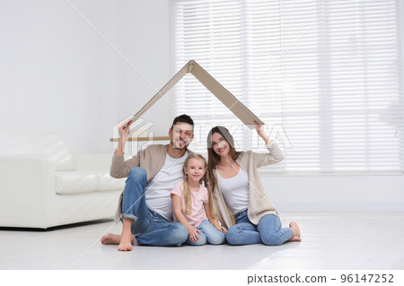 Happy family sitting under cardboard roof at home. Insurance concept 96147252