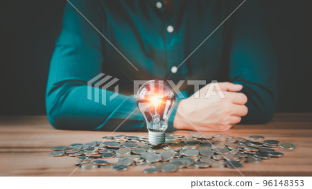 A glowing light bulb on pile money cions on a wooden table, business problem solving ideas and creative marketing ideas Inventing, save money and learning new things. A glowing light bulb on pile money cions on a wooden table, business problem solving ideas and creative marketing ideas Inventing, save money and learning new things. 96148353