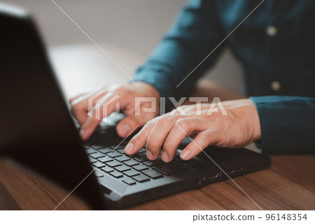 Closeup image of a young man working and typing on laptop computer keyboard on wooden table in cafe. 96148354