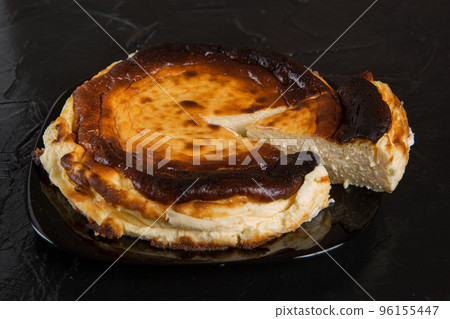 Spanish cheesecake on a black plate, on a black slate, one piece is cut off from the whole dessert Spanish cheesecake on a black plate, on a black slate, one piece is cut off from the whole dessert 96155447