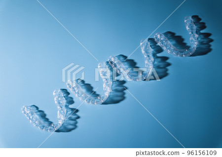 background for dental clinic or orthodontics. invisible plastic new braces lie in a row on a blue background, studio shot with shadows 96156109