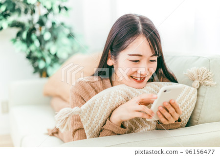 A smiling Japanese woman using a smartphone on the sofa 96156477