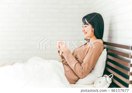 A smiling woman measuring her body temperature using a thermometer in her bedroom (cooling sheet) 96157677