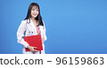 Cheerful asian woman doctor wear uniform with stethoscope holding clipboard over isolated blue 96159863