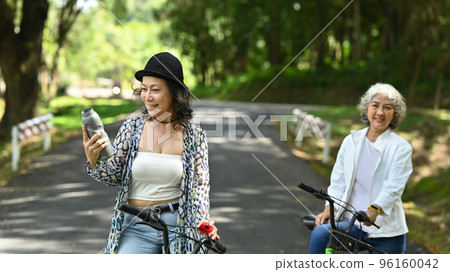 Two middle aged women best friends resting from cycling in summer park. Retirement people lifestyle, outdoor activity concept 96160042