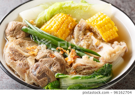 Bulalo is a Filipino boiled soup made with bone-in beef shanks, corn and cabbage leaves closeup in the bowl. Horizontal 96162704