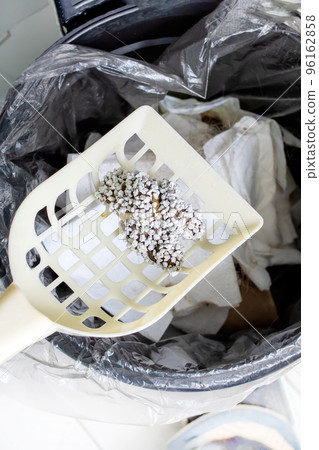 A scoop with cat excrement over a garbage can A scoop with cat excrement over a garbage can 96162858