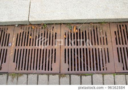 The sewer grate on the sidewalk is rusty The sewer grate on the sidewalk is rusty 96162884