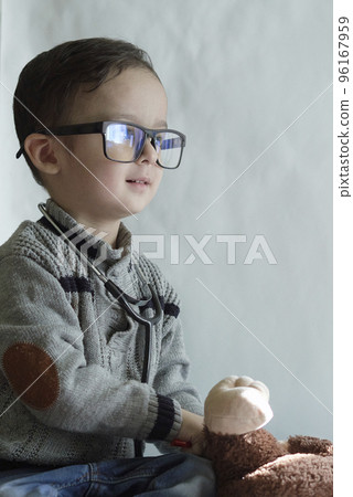 a young boy wearing glasses and playing with a stuffed bear on the floor in front of a white wall behind him a young boy wearing glasses and playing with a stuffed bear on the floor in front of a white wall behind him 96167959