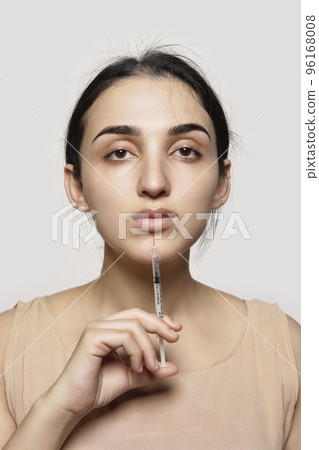 a young woman holding a sy in her right hand and looking at the camera she is wearing a beige top 96168008