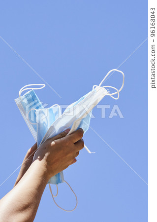 someone's hand holding a blue and white mask in the shape of a kite against a clear blue sky 96168043