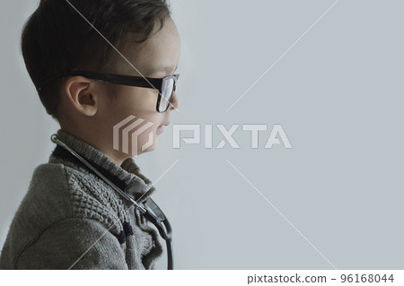 a little boy wearing glasses and looking at something on the wall with his hand in his pocket a little boy wearing glasses and looking at something on the wall with his hand in his pocket 96168044