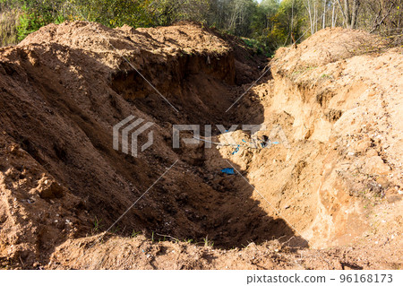 A deep trench dug in sandy soil in a forest area for laying engineering networks 96168173
