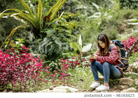 Asian woman with a backpack sitting on a rock using a mobile phone 96168825