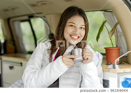 Asian woman holding a hot drink inside the campervan enjoying camp activity 96169044