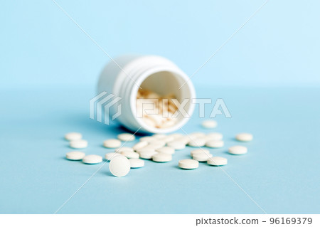 Medicine bottle and white pills spilled on a light background. Medicines and prescription pills flat lay background. White medical pills and tablets spilling out of a drug bottle 96169379