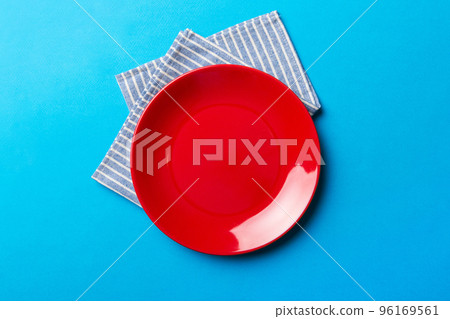Top view on colored background empty round red plate on tablecloth for food. Empty dish on napkin with space for your design Top view on colored background empty round red plate on tablecloth for food. Empty dish on napkin with space for your design 96169561