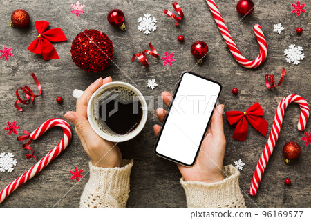 Above view of female hand holding smart phone with hot cup of coffee. Christmas decoration on colored background 96169577