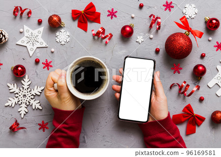 Above view of female hand holding smart phone with hot cup of coffee. Christmas decoration on colored background 96169581
