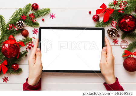 Christmas online shopping from home, female hands holding tablet pc with blank white display top view. woman hand holding tablet with blank screen, Christmas tree and gifts on background Christmas online shopping from home, female hands holding tablet pc with blank white display top view. woman hand holding tablet with blank screen, Christmas tree and gifts on background 96169583