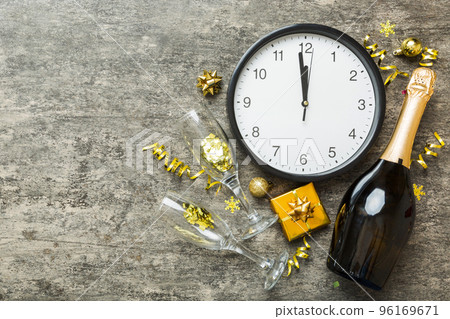 New year celebration concept with a bottle of champagne and two glasses toasting. Christmas gift box, alarm clock and fir tree branch on colored table. Top view Copy space New year celebration concept with a bottle of champagne and two glasses toasting. Christmas gift box, alarm clock and fir tree branch on colored table. Top view Copy space 96169671
