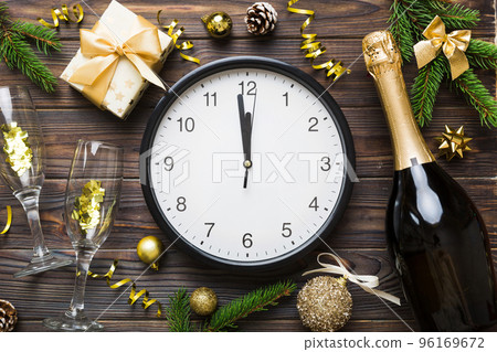New year celebration concept with a bottle of champagne and two glasses toasting. Christmas gift box, alarm clock and fir tree branch on colored table. Top view Copy space New year celebration concept with a bottle of champagne and two glasses toasting. Christmas gift box, alarm clock and fir tree branch on colored table. Top view Copy space 96169672