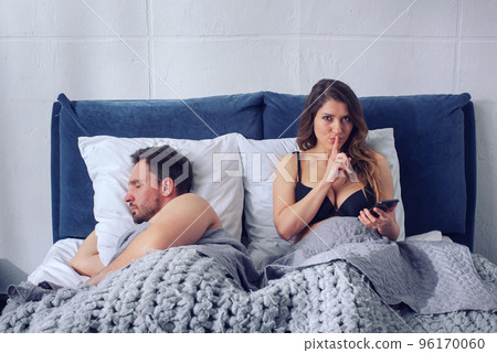Girlfriend secretly chatting with others while he sleeps. Infidelity concept Girlfriend secretly chatting with others while he sleeps. Infidelity concept 96170060