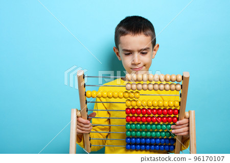 Child tries to solve mathematical problem with abacus. Cyan background Child tries to solve mathematical problem with abacus. Cyan background 96170107