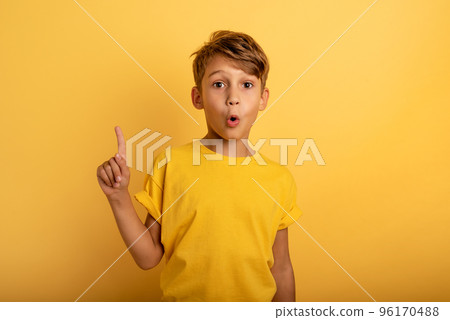 Child indicates above. Amazed and shocked expression. Yellow background 96170488