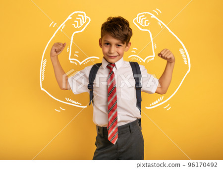 Young boy student acts like a muscled man. Yellow background 96170492