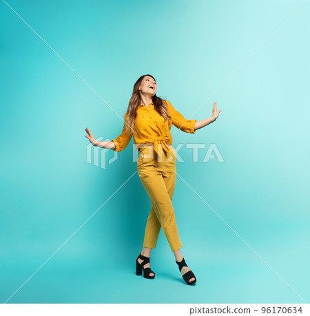 Brunette girl with a yellow clothes walks over a cyan background. Concept of fashion and shopping with joyful expression Brunette girl with a yellow clothes walks over a cyan background. Concept of fashion and shopping with joyful expression 96170634