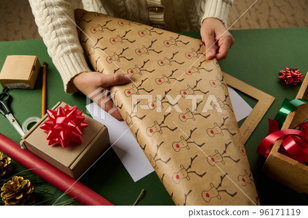 Details: woman's hands rolling out a wrapping gift paper with deer pattern, packing presents for Christmas or New Year. Boxing Day. New Year and Xmas preparations. Happy winter holidays. Diy presents 96171119