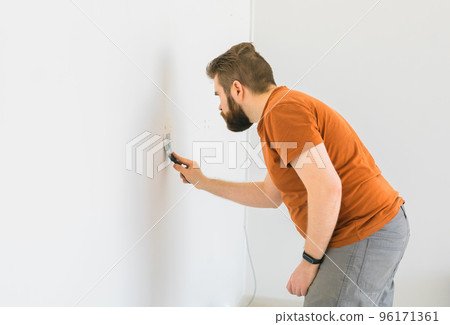 Man smoothes wall surface with a wall grinder. Male grind a white plaster wall - renovation and redecoration concept Man smoothes wall surface with a wall grinder. Male grind a white plaster wall - renovation and redecoration concept 96171361