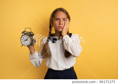 Young child student with ringing alarm clock is lazy going to school. Yellow background Young child student with ringing alarm clock is lazy going to school. Yellow background 96171375