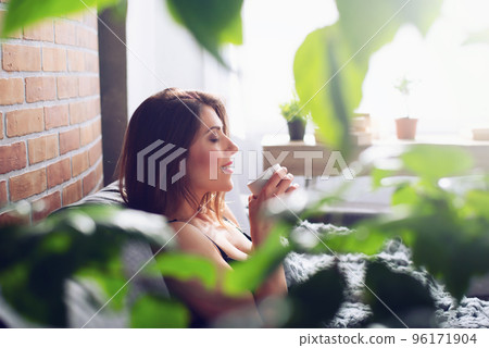 Brunette girl drinking cappuccino for breakfast on a sofa. Concept of relax Brunette girl drinking cappuccino for breakfast on a sofa. Concept of relax 96171904