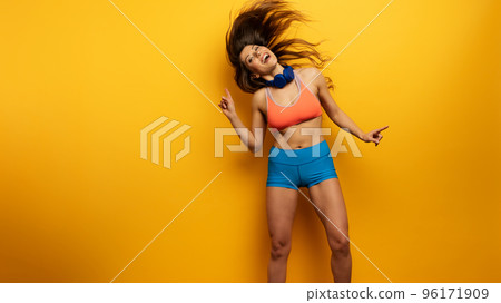 Fitness girl listens to music with headset. Joyful and happy expression on yellow background Fitness girl listens to music with headset. Joyful and happy expression on yellow background 96171909