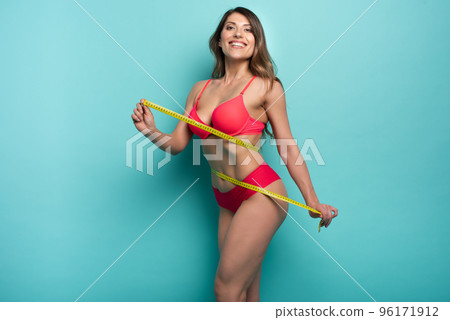 Girl measures with the meter the diet results. Happy and joyful expression. Cyan background 96171912
