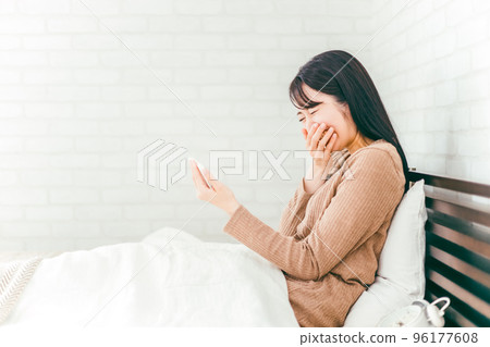 Japanese woman laughing out loud watching videos and movies on her smartphone in her bedroom 96177608